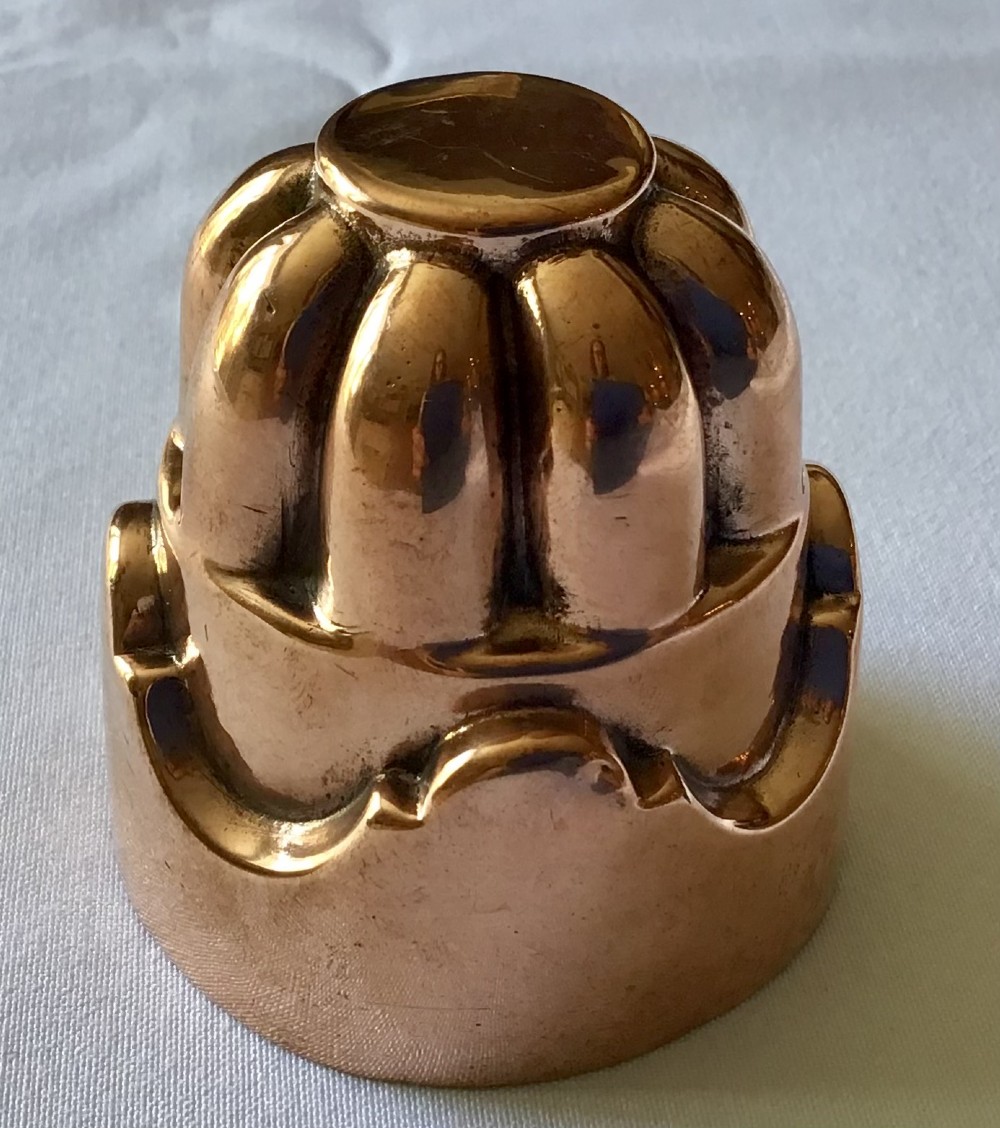 A small polished copper jelly mould featuring a two-tiered design with fluted vertical lobes on the upper section and a scalloped base.