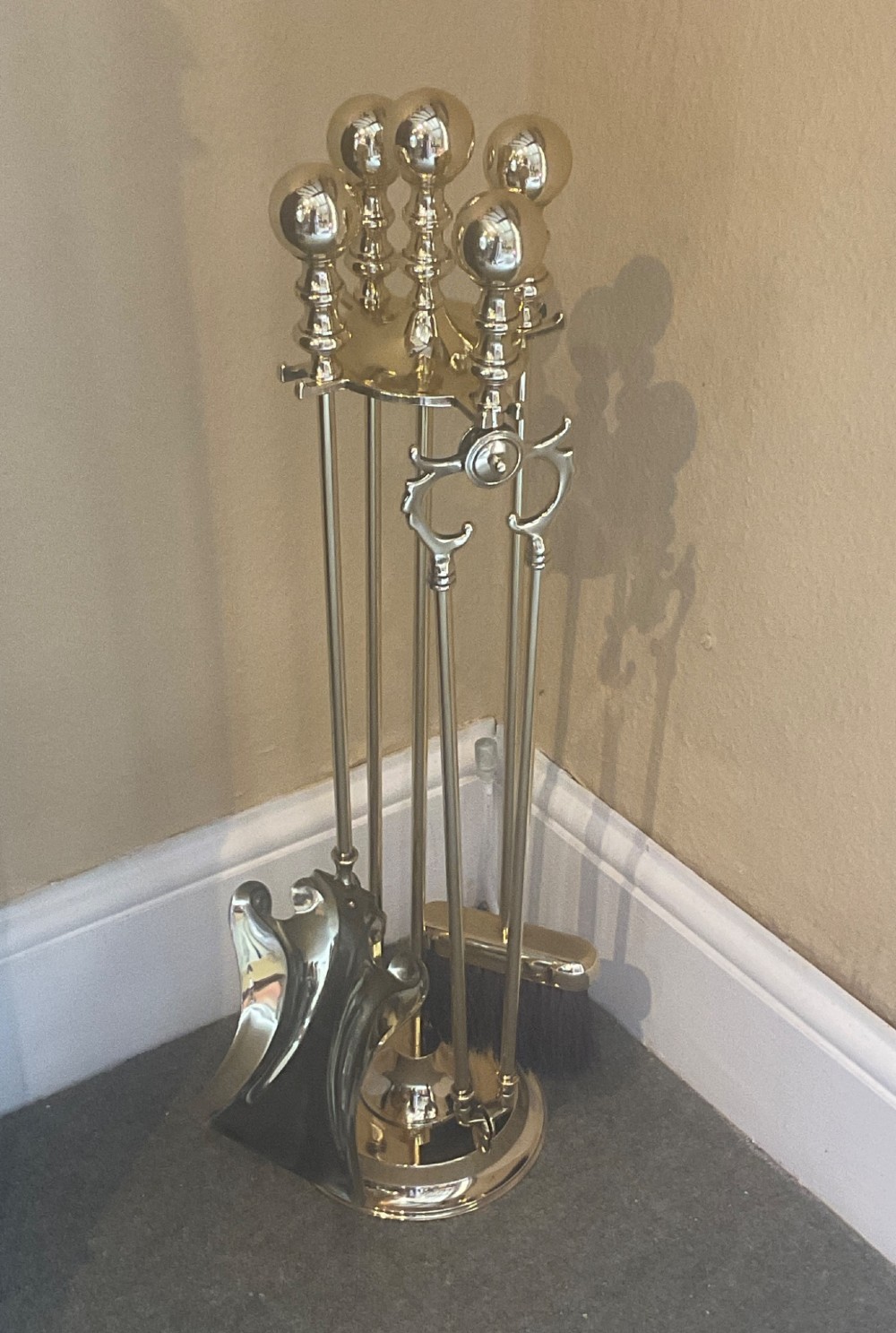 A polished brass companion set featuring a central stand with sphere finials holding a shovel, tongs, poker, and hearth brush.