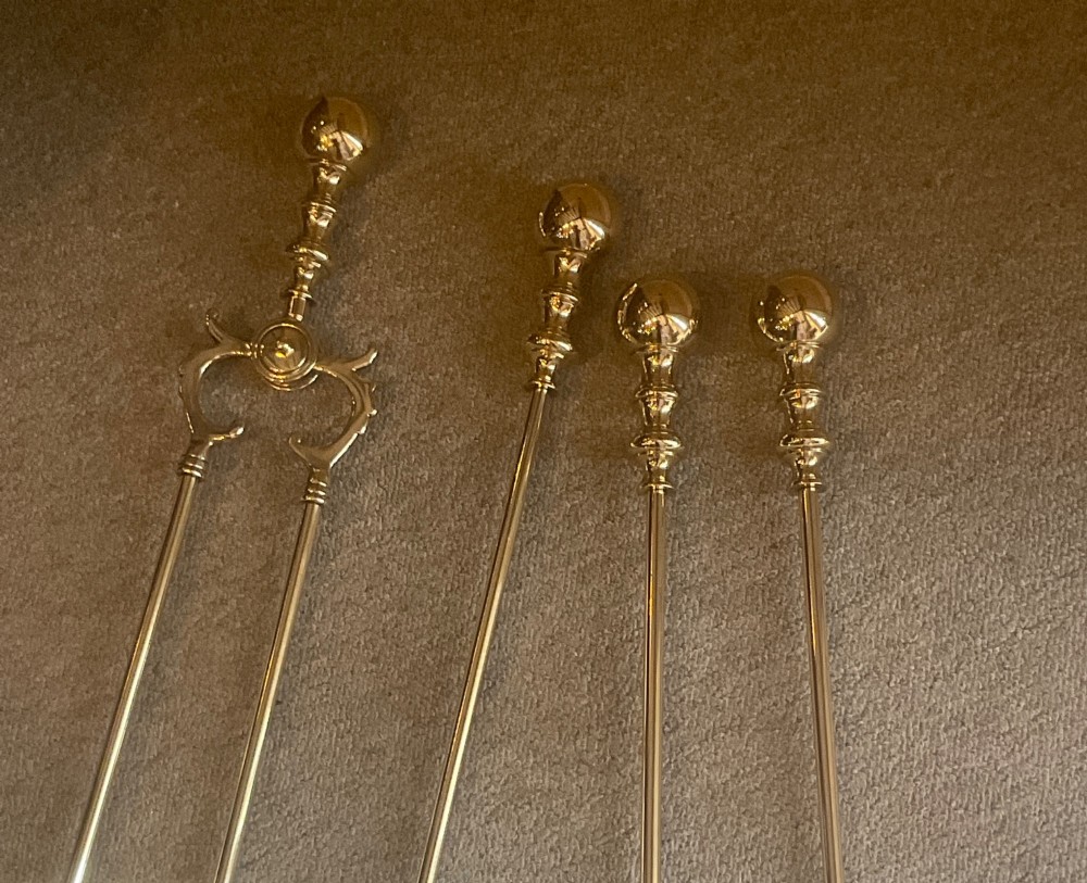 A polished brass companion set featuring a central stand with sphere finials holding a shovel, tongs, poker, and hearth brush. View V