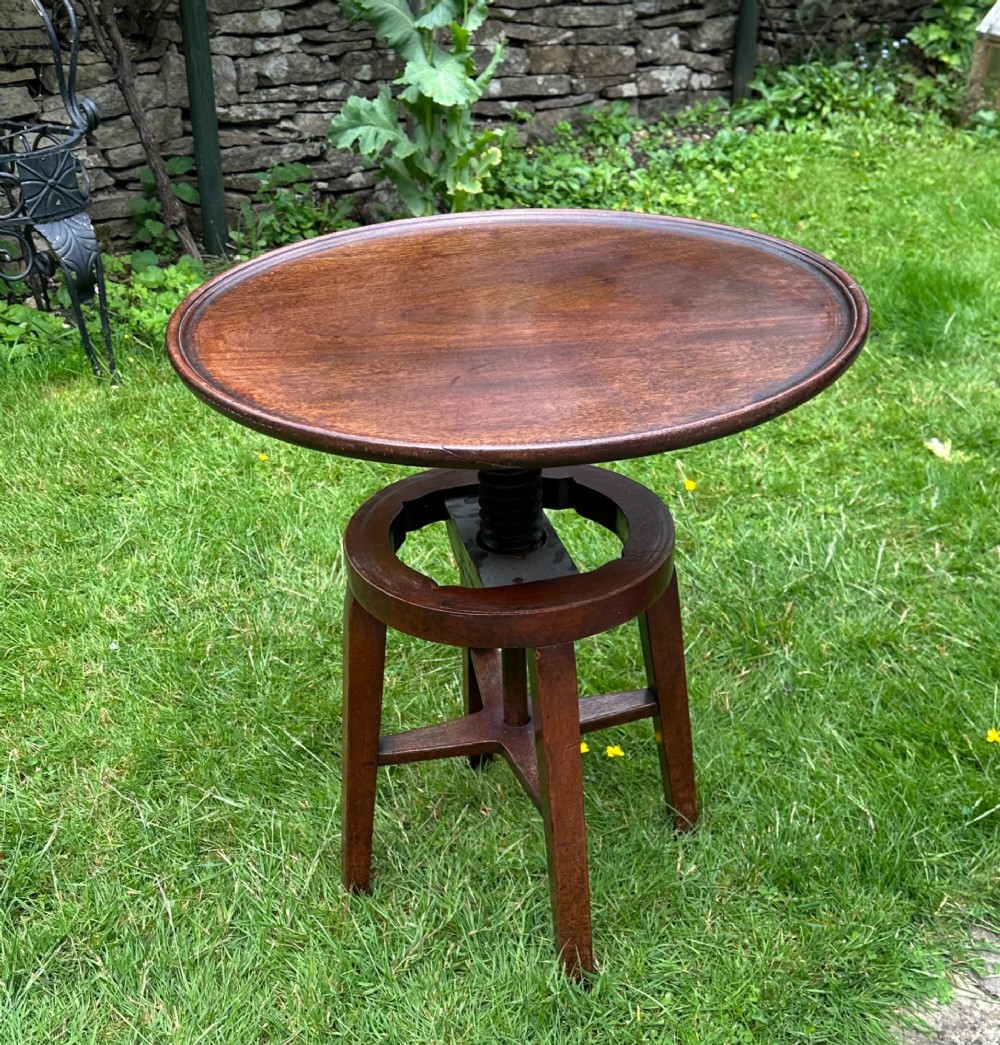 An antique round mahogany wine table with a moulded top and a threaded height-adjusting central screw resting on four legs.