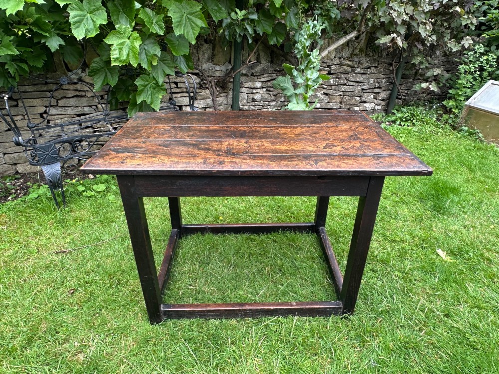 An antique dark brown oak table featuring a plank top surface, square legs, and low box stretchers.