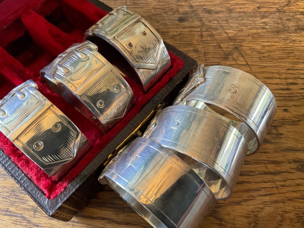 A set of six silver napkin rings styled like belt buckles presented inside a red velvet-lined presentation case. View V
