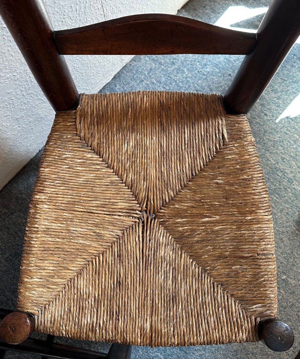 A pair of dark oak antique chapel chairs featuring woven rush seats, ladder back splats, and integrated top book ledges. View IV