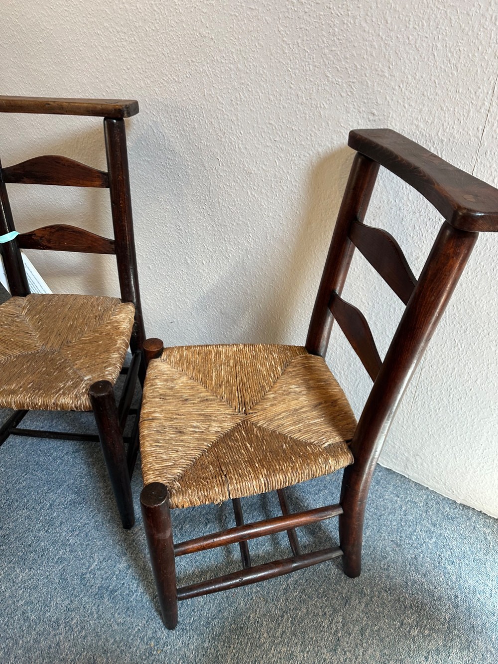 A pair of dark oak antique chapel chairs featuring woven rush seats, ladder back splats, and integrated top book ledges. View VII
