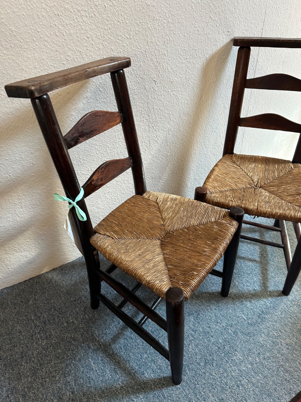 A pair of dark oak antique chapel chairs featuring woven rush seats, ladder back splats, and integrated top book ledges. View VIII