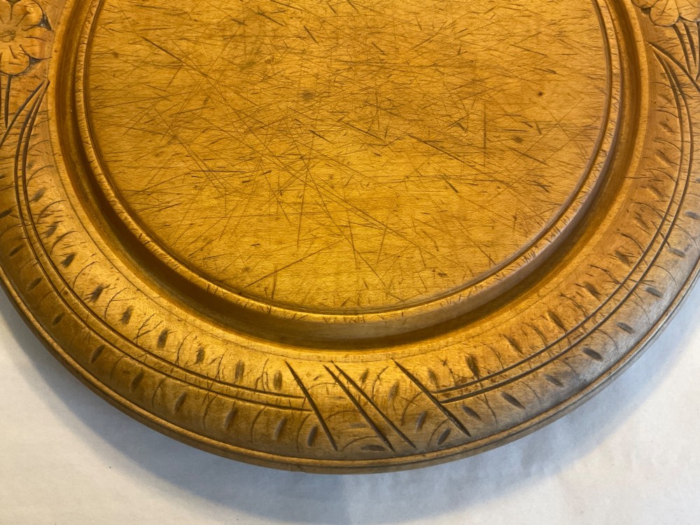 A circular antique carved wooden bread board featuring the word BREAD in relief alongside carved floral motifs around the border and knife marks in the centre. View IV