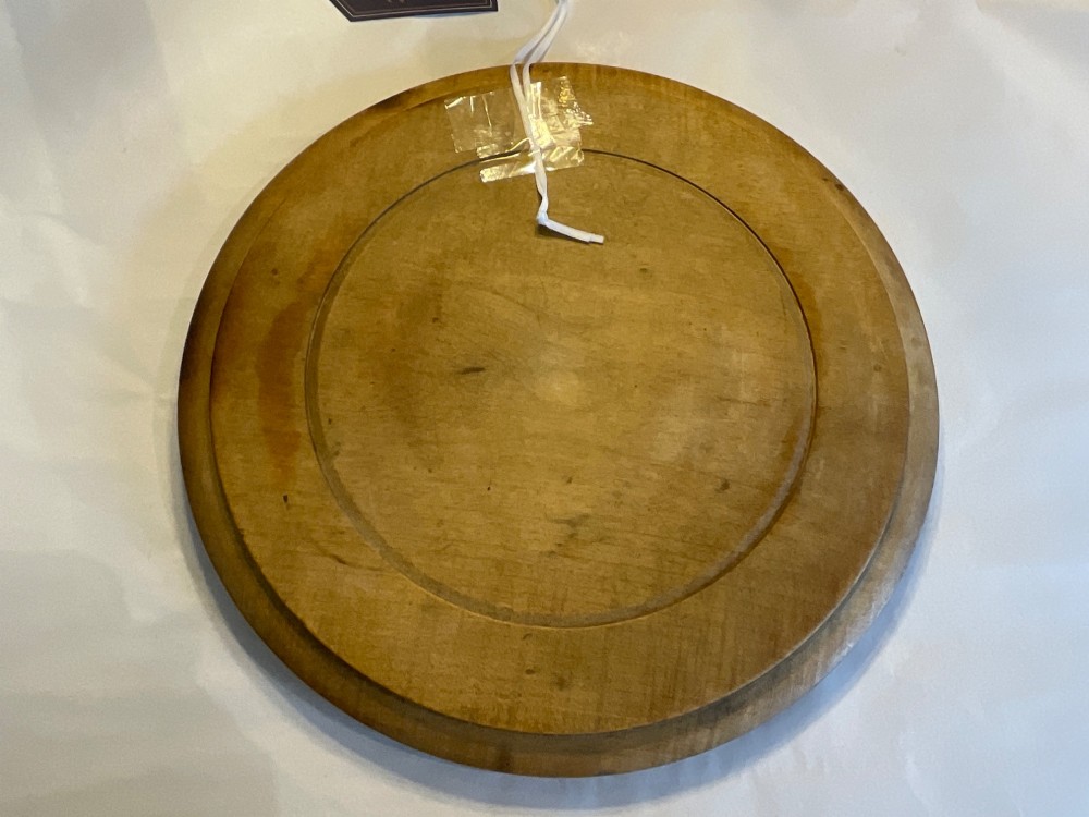 A circular antique carved wooden bread board featuring the word BREAD in relief alongside carved floral motifs around the border and knife marks in the centre. View V