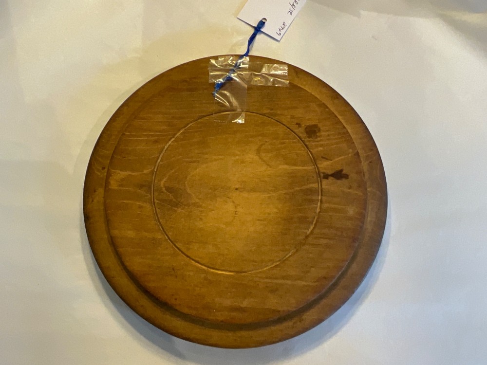 A circular antique wooden bread board featuring hand-carved lettering reading BREAD along the upper rim and knife marks across the centre. View VI