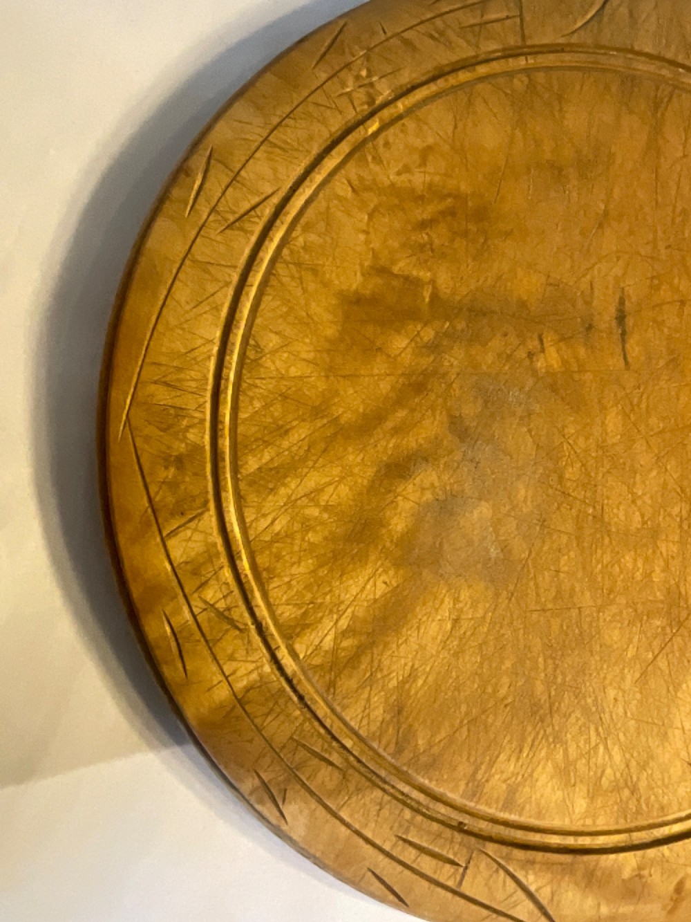 A circular carved wooden bread board with carved lettering spelling BREAD along the outer rim and visible knife marks. View III