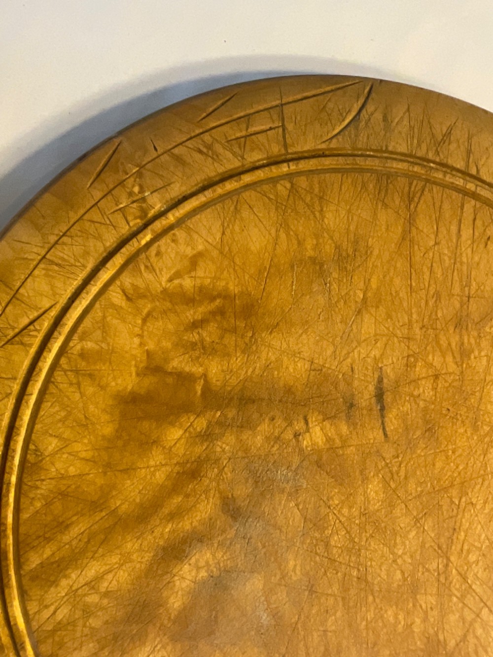 A circular carved wooden bread board with carved lettering spelling BREAD along the outer rim and visible knife marks. View IV