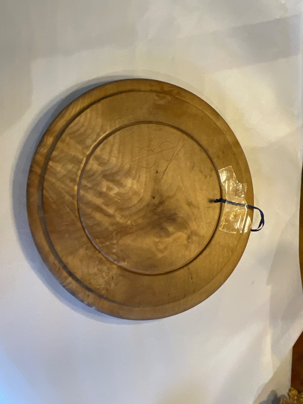 A circular carved wooden bread board with carved lettering spelling BREAD along the outer rim and visible knife marks. View V
