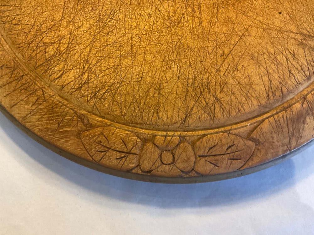 A circular antique carved wooden bread board featuring the word Bread carved into the upper border, leaf motifs carved on the lower border, and central knife marks from usage. View III