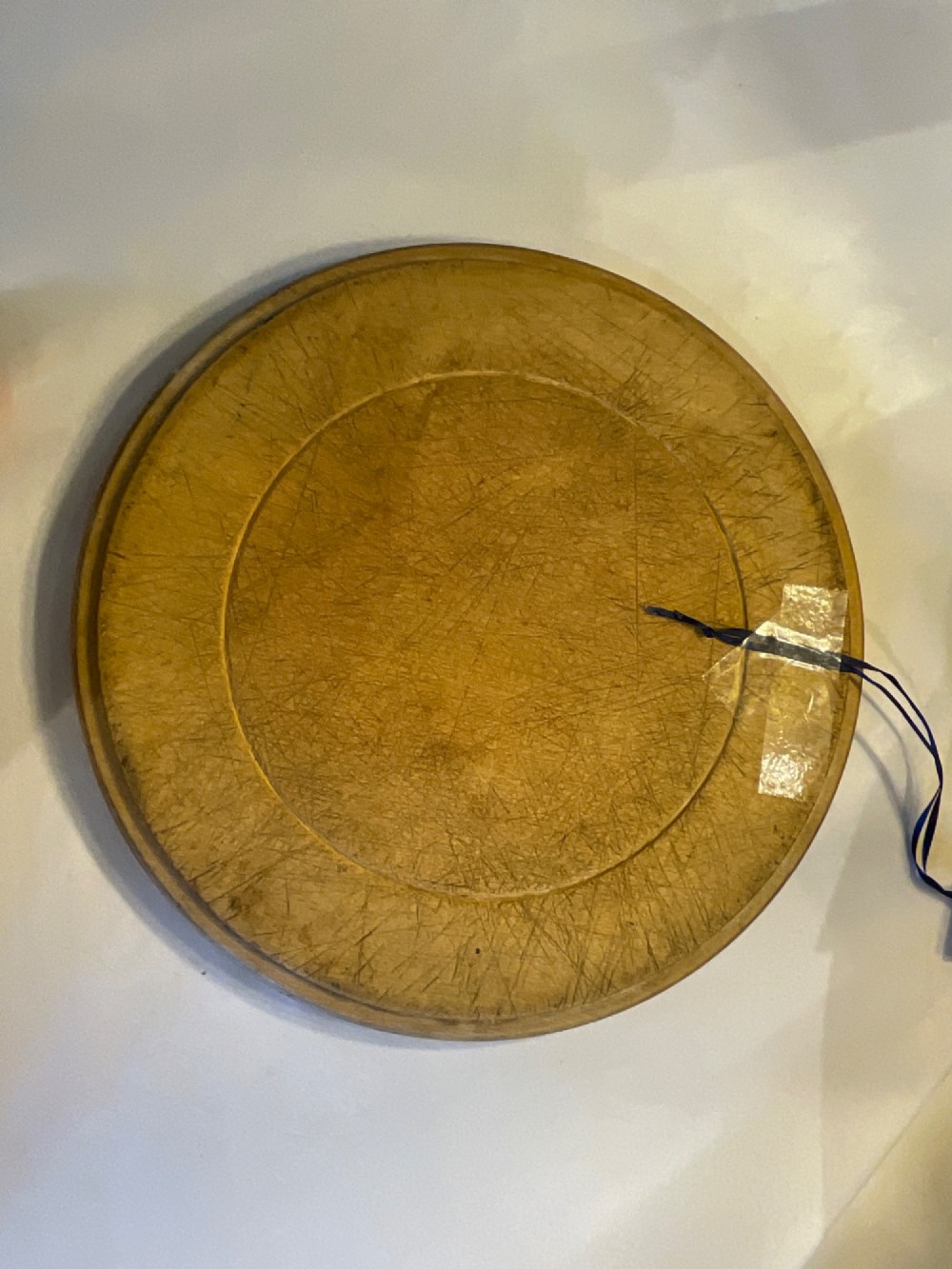 A circular antique carved wooden bread board featuring the word Bread carved into the upper border, leaf motifs carved on the lower border, and central knife marks from usage. View IV