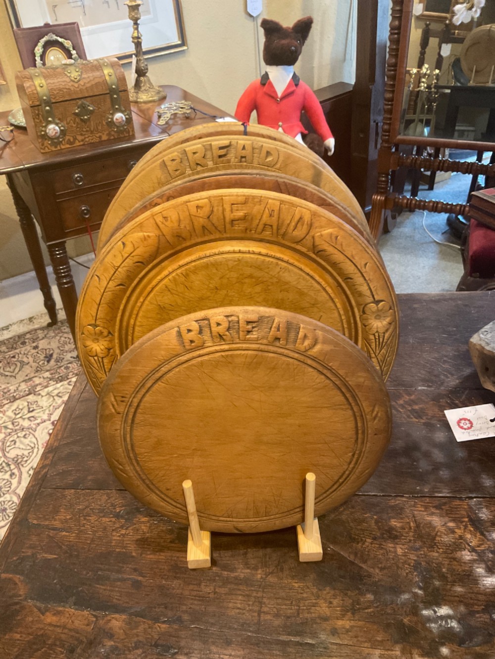 A circular antique carved wooden bread board featuring the word Bread carved into the upper border, leaf motifs carved on the lower border, and central knife marks from usage. View V