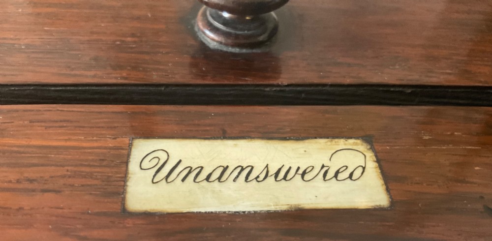 A dark mahogany 19th-century letter box featuring two top slots labelled Answered and Unanswered, a turned central knob, and a front keyhole with an inserted key. View III