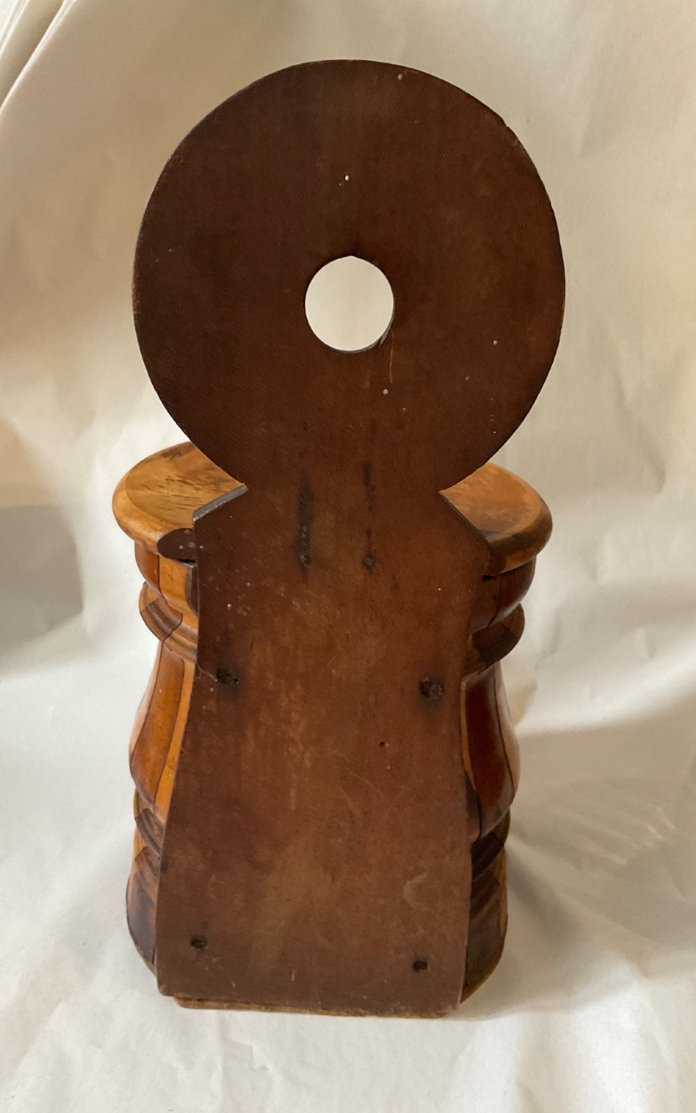 A mid-nineteenth century coopered wooden salt box featuring alternating dark and light timber staves, a circular hinged lid, and an arched backplate with a hanging aperture. View III