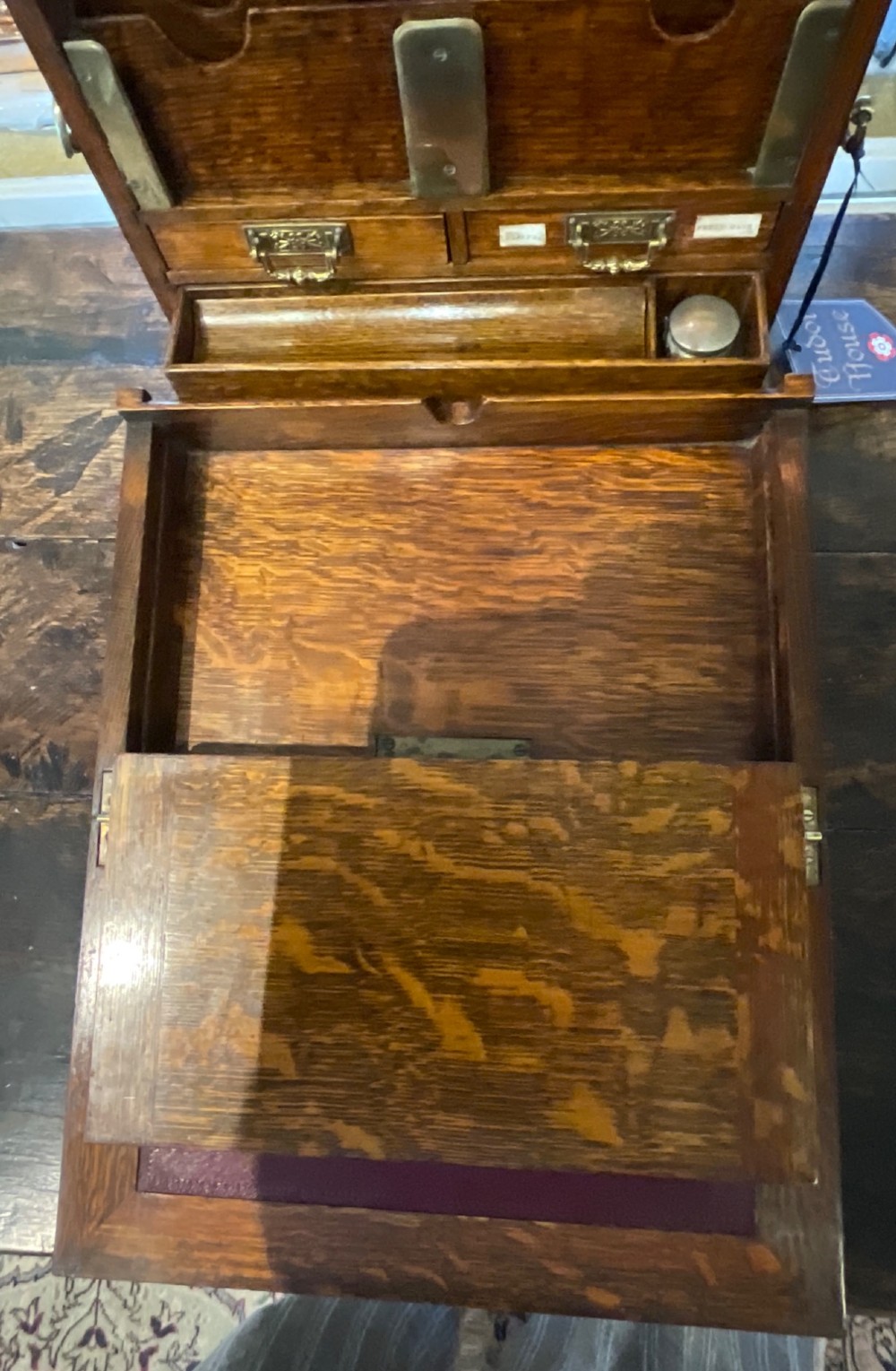 An open Victorian oak stationery box featuring internal tiered letter slots, two small drawers, a pen tray, a folding writing slope, and brass fittings. View V