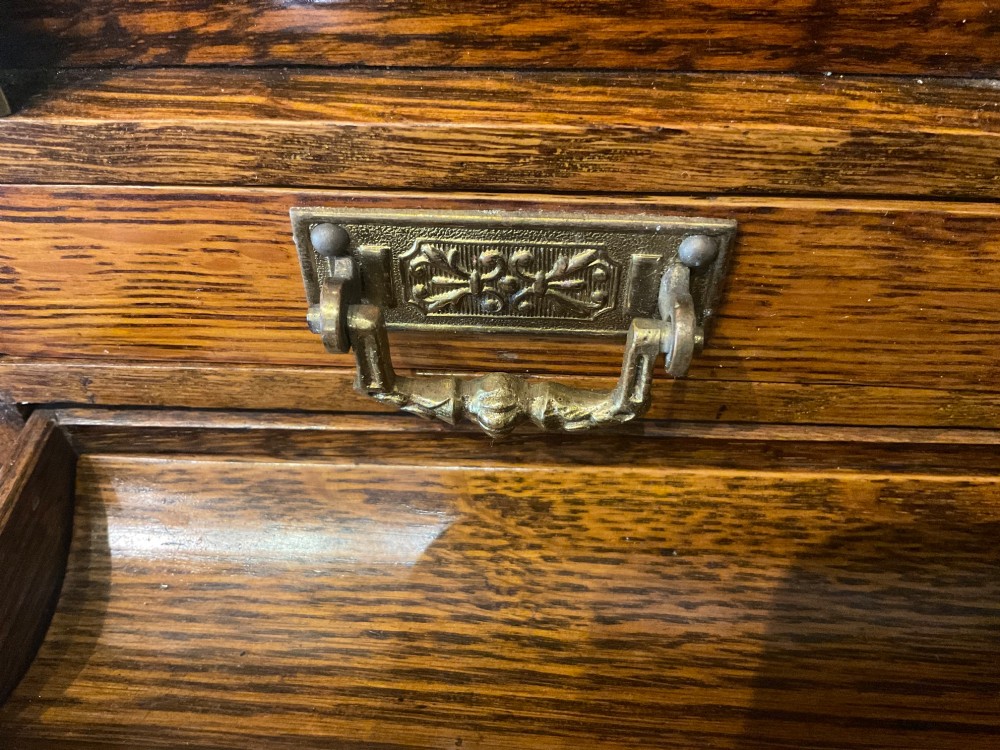 An open Victorian oak stationery box featuring internal tiered letter slots, two small drawers, a pen tray, a folding writing slope, and brass fittings. View VI