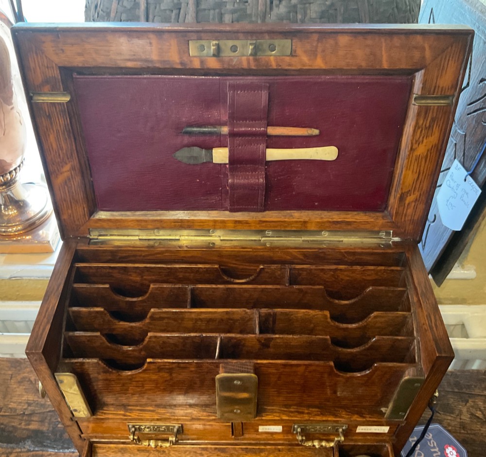 An open Victorian oak stationery box featuring internal tiered letter slots, two small drawers, a pen tray, a folding writing slope, and brass fittings. View VII