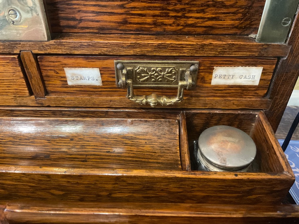 An open Victorian oak stationery box featuring internal tiered letter slots, two small drawers, a pen tray, a folding writing slope, and brass fittings. View IX