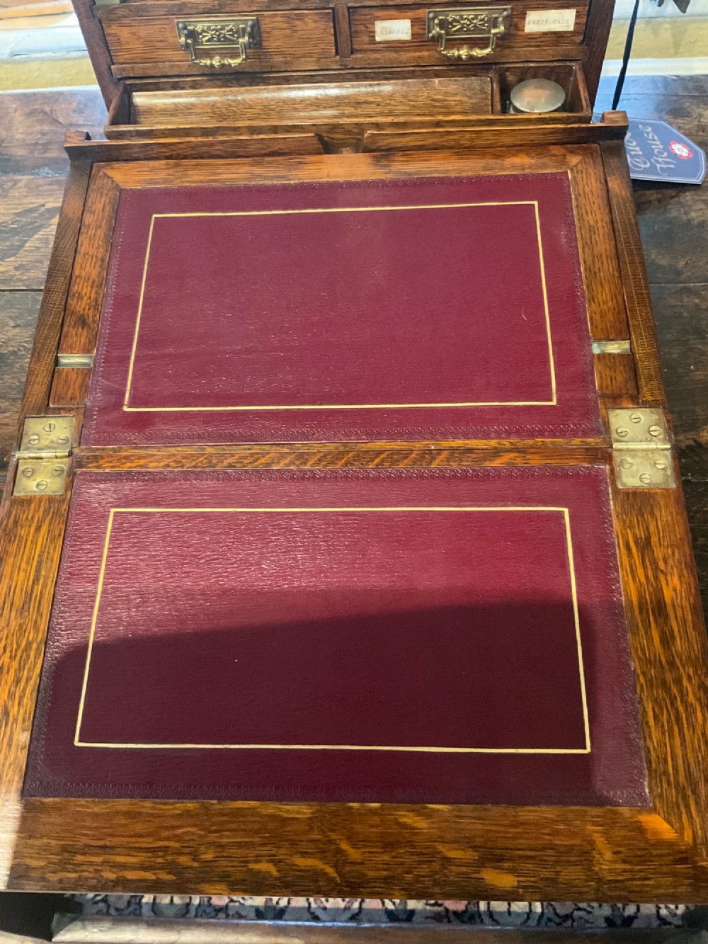 An open Victorian oak stationery box featuring internal tiered letter slots, two small drawers, a pen tray, a folding writing slope, and brass fittings. View X