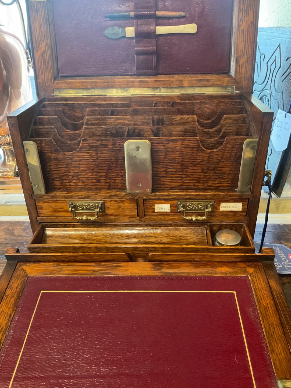An open Victorian oak stationery box featuring internal tiered letter slots, two small drawers, a pen tray, a folding writing slope, and brass fittings. View XI