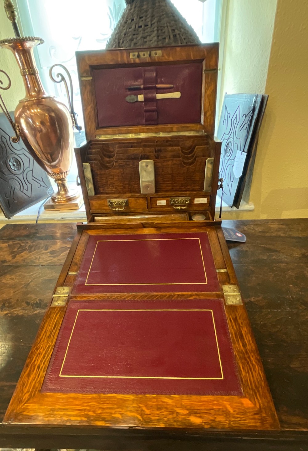 An open Victorian oak stationery box featuring internal tiered letter slots, two small drawers, a pen tray, a folding writing slope, and brass fittings. View XII