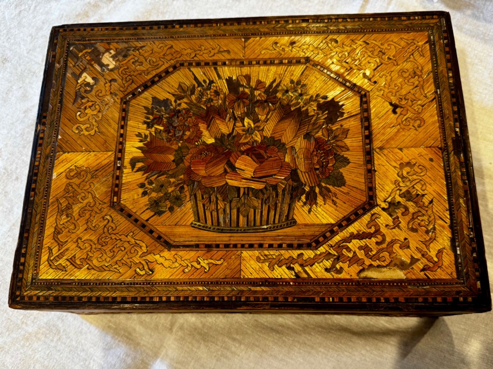 An antique rectangular wooden box embellished with straw marquetry forming a central floral basket surrounded by intricate decorative borders in golden yellow and brown shades. View IV