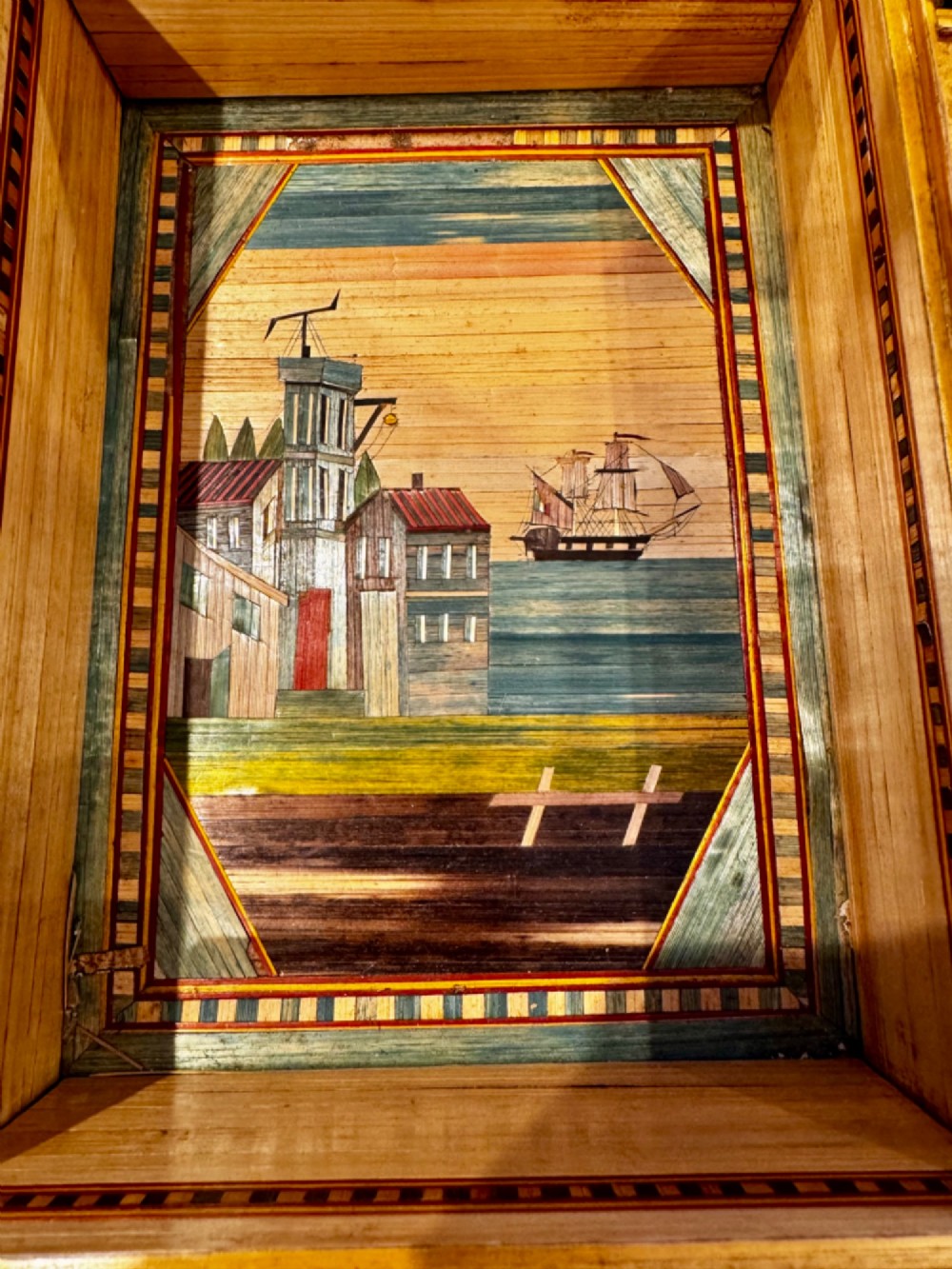 An antique rectangular wooden box embellished with straw marquetry forming a central floral basket surrounded by intricate decorative borders in golden yellow and brown shades. View VI