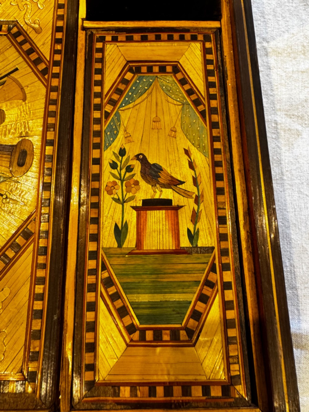 An antique rectangular wooden box embellished with straw marquetry forming a central floral basket surrounded by intricate decorative borders in golden yellow and brown shades. View VIII