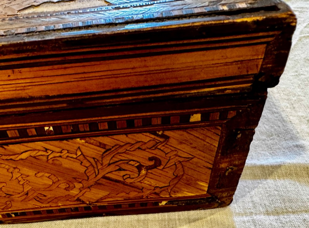 An antique rectangular wooden box embellished with straw marquetry forming a central floral basket surrounded by intricate decorative borders in golden yellow and brown shades. View XIV