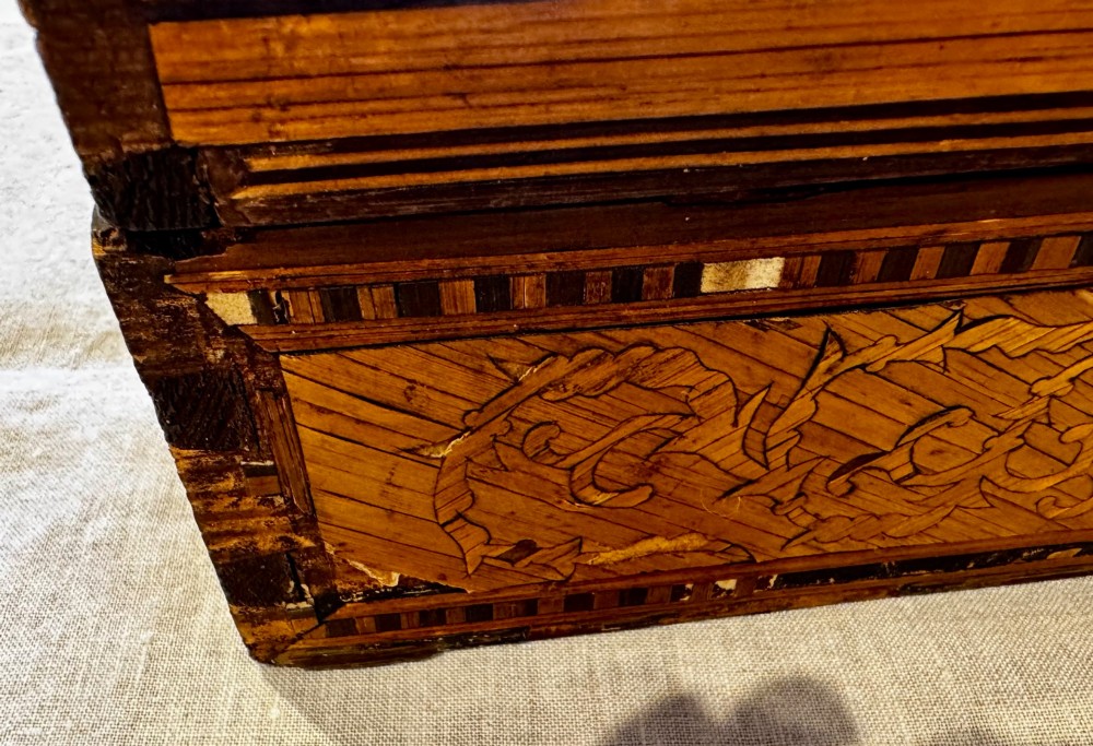 An antique rectangular wooden box embellished with straw marquetry forming a central floral basket surrounded by intricate decorative borders in golden yellow and brown shades. View XV