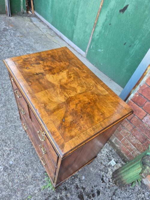 fig 2. A small burr walnut bachelors chest featuring four drawers with brass handles, a brushing slide, and bracket feet.