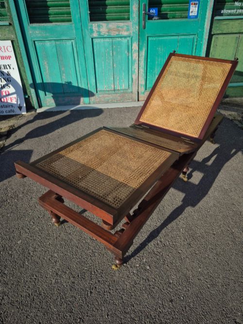 fig 1. An antique campaign-style daybed crafted from dark timber with three woven cane panels, adjustable reclining sections, turned legs, and brass castors.