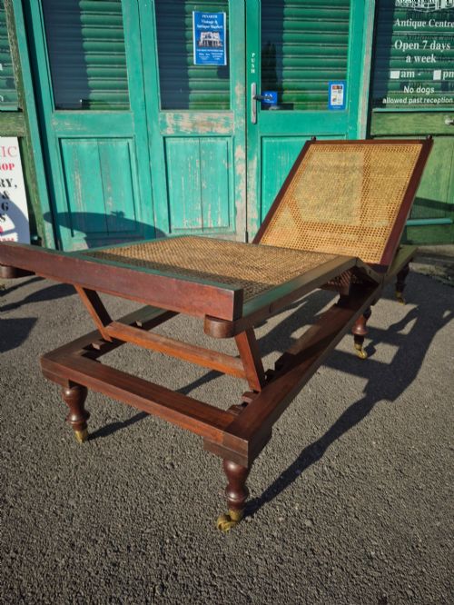 fig 3. An antique campaign-style daybed crafted from dark timber with three woven cane panels, adjustable reclining sections, turned legs, and brass castors.