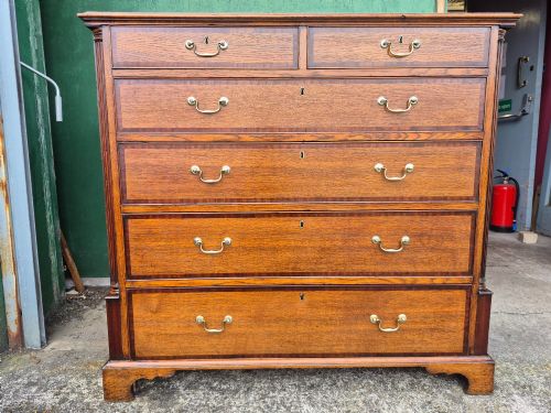 fig 1. A golden oak Georgian chest of drawers featuring two short drawers over three long drawers with brass handles, reeded side columns, and bracket feet.