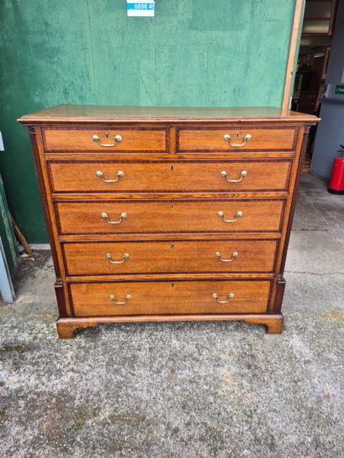 fig 2. A golden oak Georgian chest of drawers featuring two short drawers over three long drawers with brass handles, reeded side columns, and bracket feet.