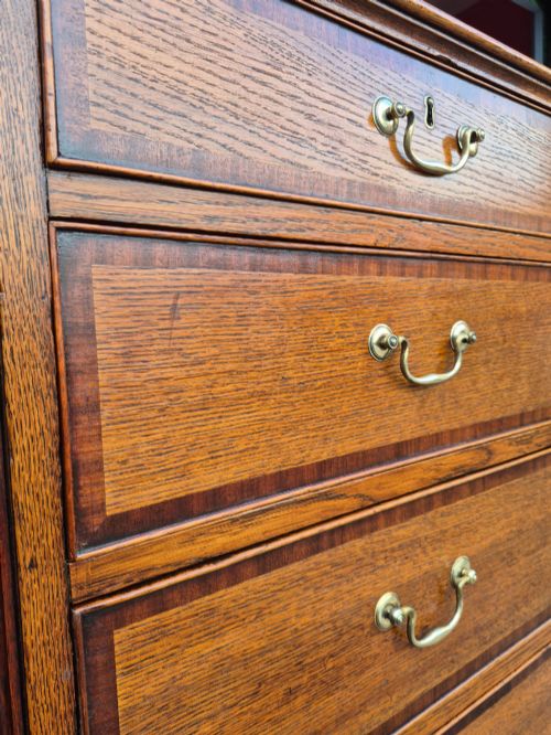 fig 4. A golden oak Georgian chest of drawers featuring two short drawers over three long drawers with brass handles, reeded side columns, and bracket feet.