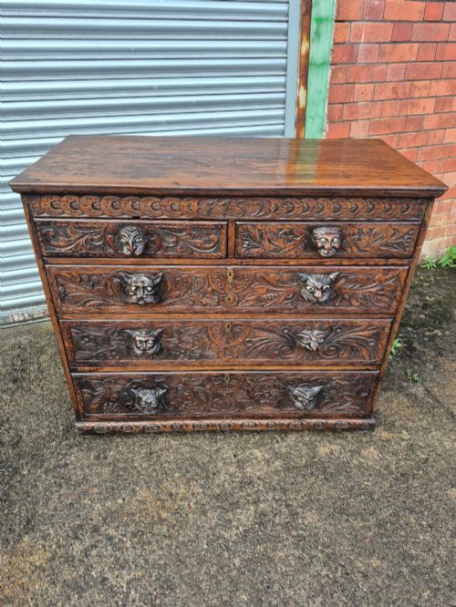 fig 1. A nineteenth-century dark oak chest of drawers featuring hand-carved grotesque Green Man face masks and elaborate foliate scrollwork across the front.