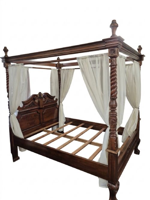 fig 1. A dark hardwood queen-size four-poster bed frame featuring turned posts, a detailed carved headboard, and draped cream fabric.