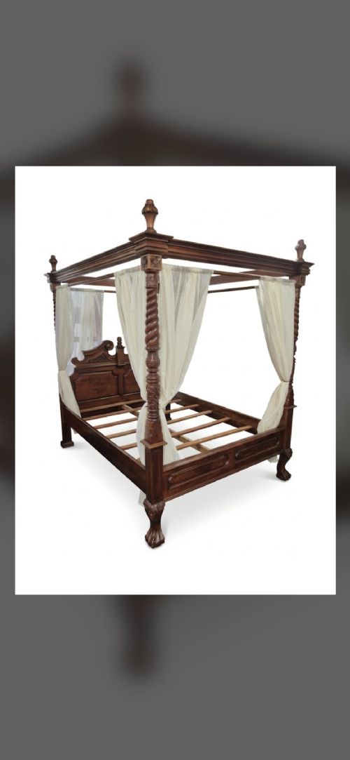 fig 2. A dark hardwood queen-size four-poster bed frame featuring turned posts, a detailed carved headboard, and draped cream fabric.