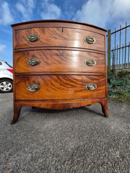fig 1. A Regency period bowfront chest of drawers crafted from flame mahogany veneer with three drawers and brass oval handles.