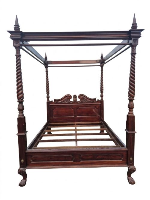 fig 1. A dark mahogany four-poster bed frame featuring four spiral barley-twist posts topped with finials, a carved headboard, and claw-and-ball feet.