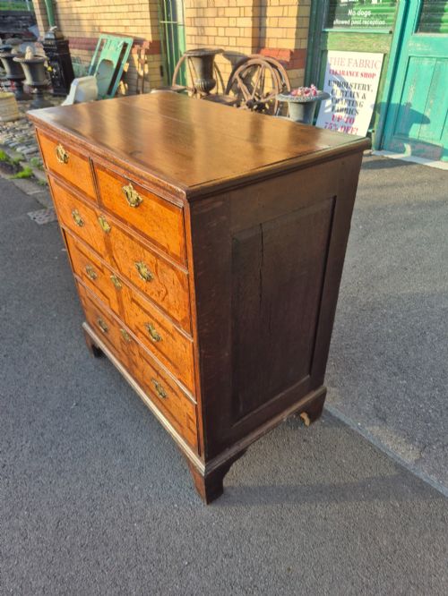 fig 2. An Early Georgian oak and walnut chest of drawers featuring geometric wood banding, engraved brass handles, and bracket feet.