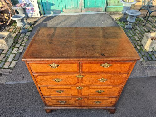 fig 5. An Early Georgian oak and walnut chest of drawers featuring geometric wood banding, engraved brass handles, and bracket feet.