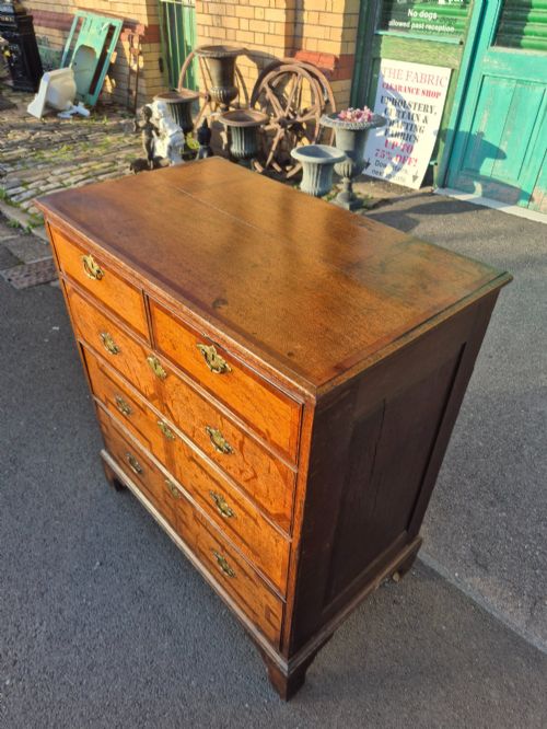 fig 6. An Early Georgian oak and walnut chest of drawers featuring geometric wood banding, engraved brass handles, and bracket feet.