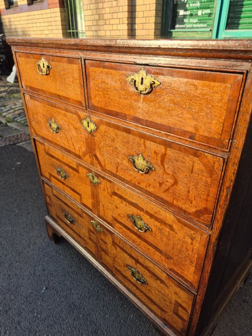 fig 7. An Early Georgian oak and walnut chest of drawers featuring geometric wood banding, engraved brass handles, and bracket feet.