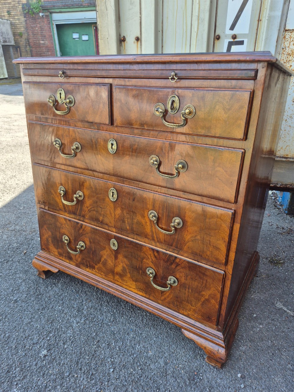 An 18th-century Georgian walnut bachelors chest featuring a brushing slide, four graduated drawers with brass handles, and bracket feet.
