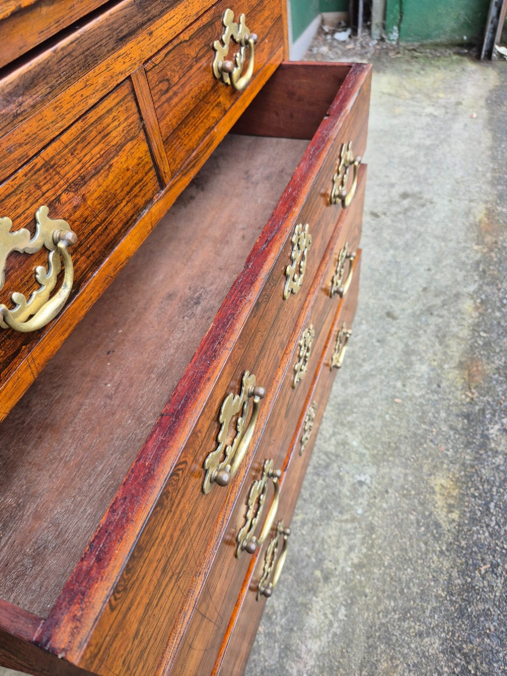 A small rosewood chest of drawers featuring brass handles, bracket feet, and a pull-out brushing slide. View VI