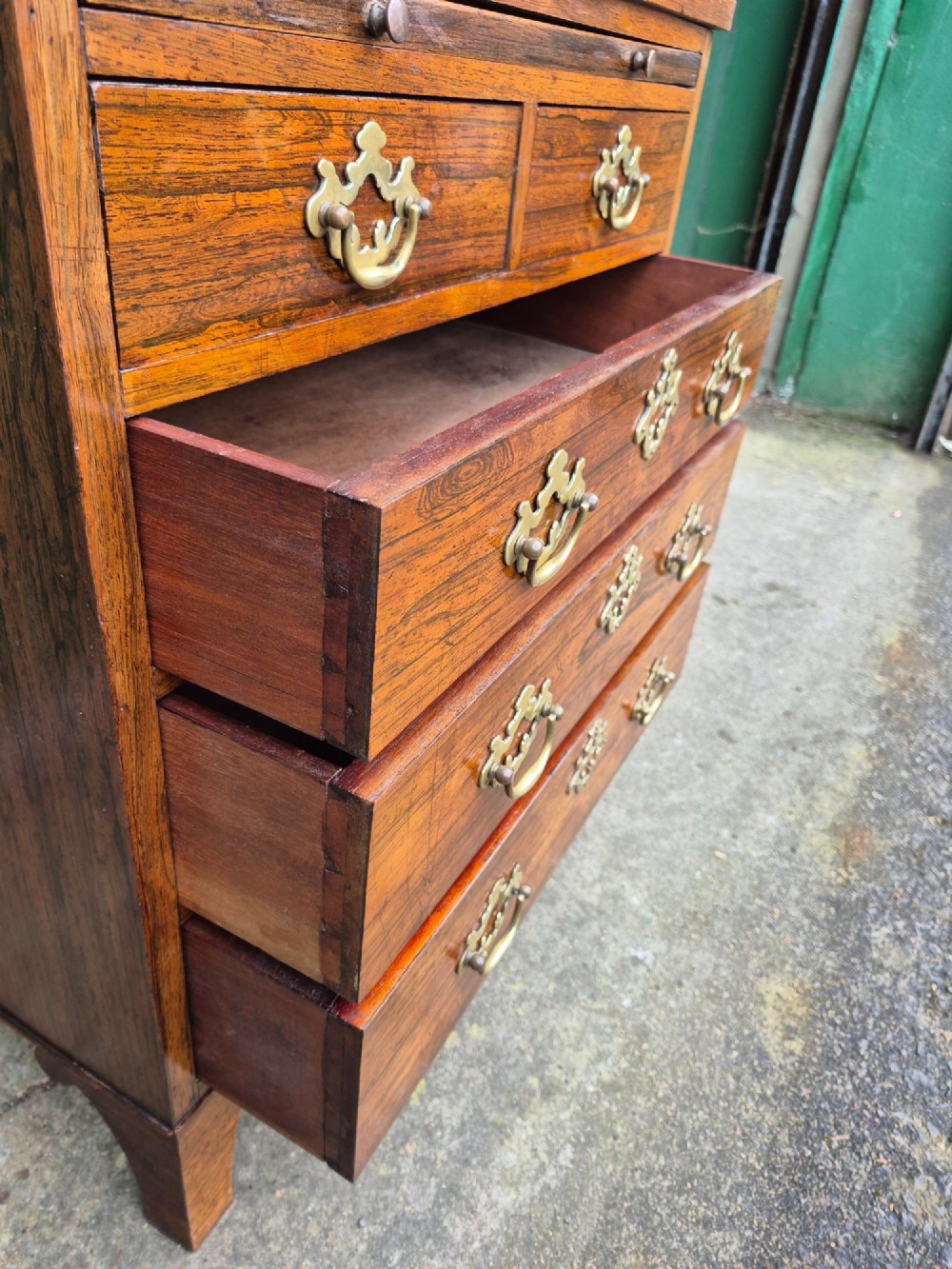 A small rosewood chest of drawers featuring brass handles, bracket feet, and a pull-out brushing slide. View VII